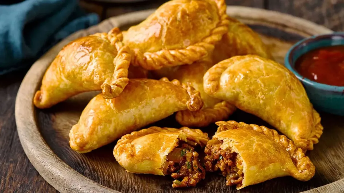 Golden baked Argentine empanadas filled with seasoned beef on a rustic wooden plate — a traditional comfort food from Argentina. Golden baked Argentine empanadas filled with seasoned beef on a rustic wooden plate — a traditional comfort food from Argentina.