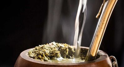 Close-up of a cured mate gourd filled with yerba mate, with hot water being poured and a bombilla inside, showing a ready-to-use mate. Close-up of a cured mate gourd filled with yerba mate, with hot water being poured and a bombilla inside, showing a ready-to-use mate.