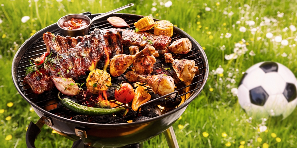 American-style BBQ with grilled ribs, chicken, vegetables, and corn on a charcoal grill outdoors on a sunny day.