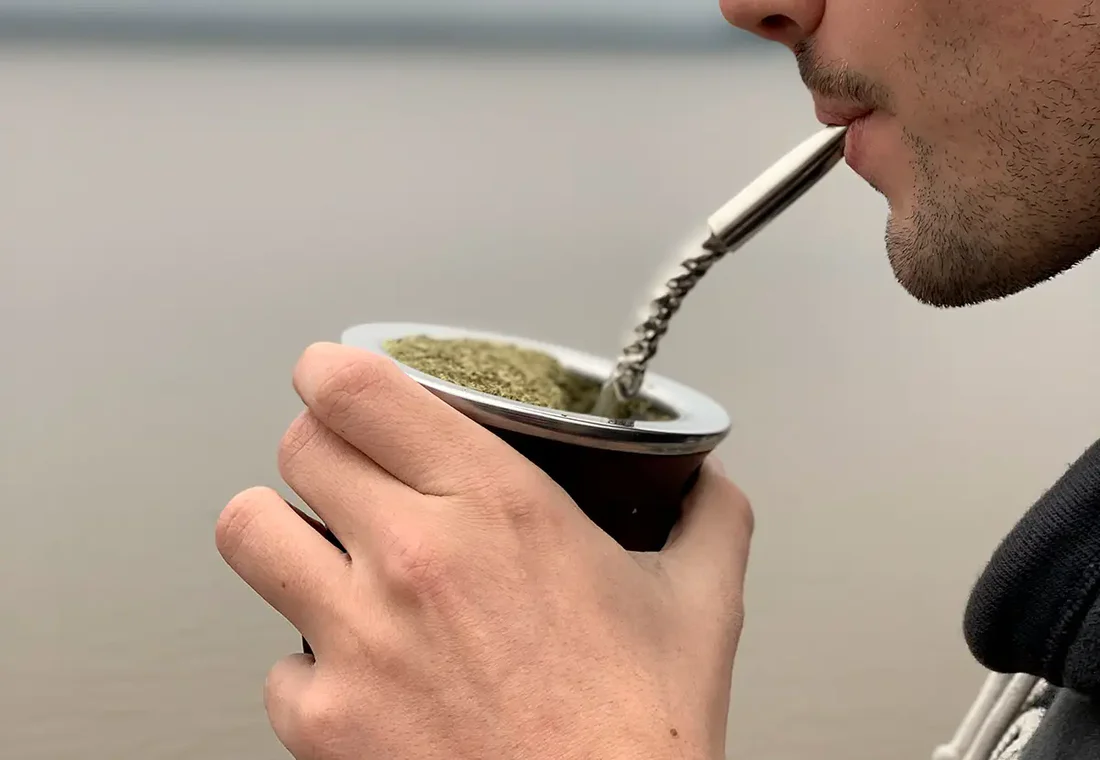 Persona tomando mate con una bombilla de metal, sosteniendo el mate con ambas manos — vista de cerca de la tradicional infusión sudamericana.