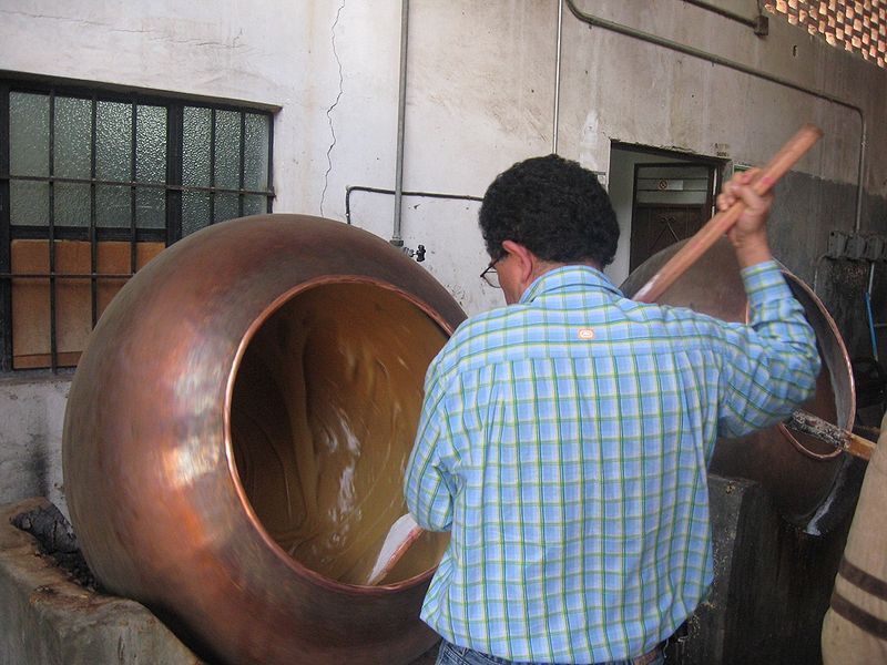 Elaboración artesanal de dulce de leche en olla de cobre, hombre revolviendo la mezcla