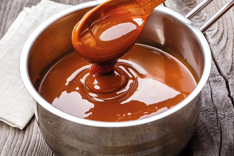 Homemade Argentinian dulce de leche being stirred in stainless steel pot with wooden spoon.