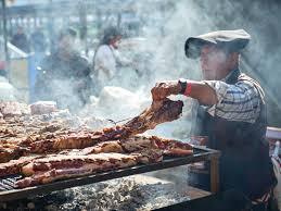 Argentinian asador grilling beef ribs over open flames at a traditional outdoor parrilla, surrounded by smoke and fire.