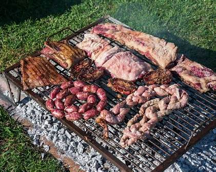 Traditional Argentinian asado with beef ribs, sausages, and organ meats grilling over wood embers on an open parrilla outdoors.