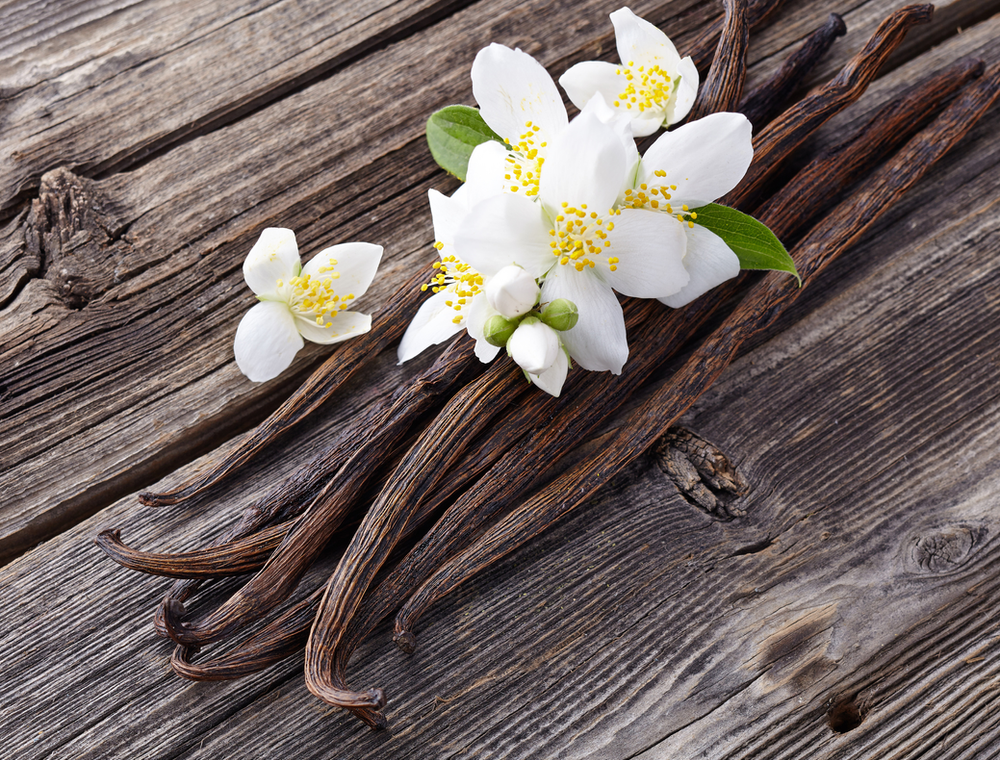 Vainas de vainilla natural con flores blancas sobre fondo de madera rústica